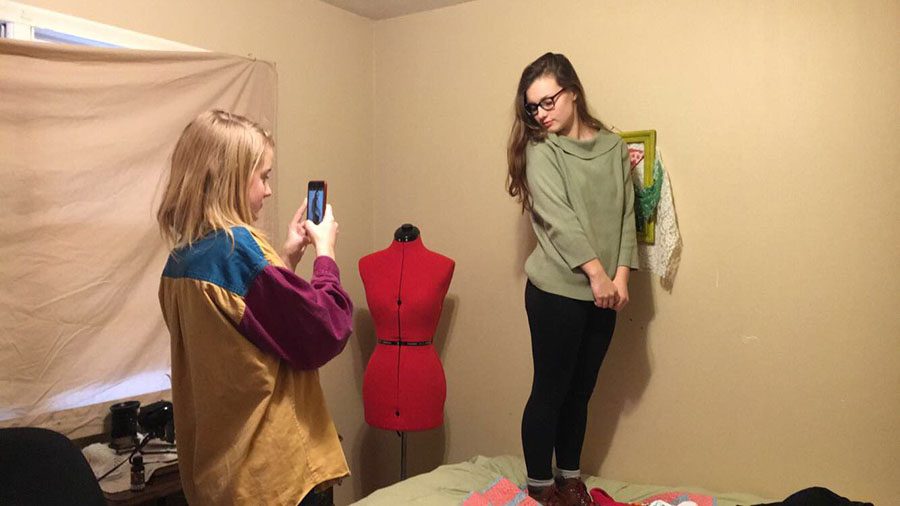 Quinn Rhodes takes a picture of Rebekah Nelson showing off a green sweater for their Twitter page. 