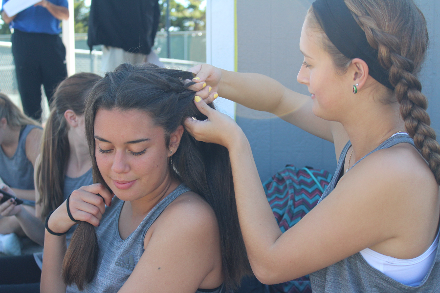 Prepping for the matches ahead seniors Kailei Sidebottom and Claudia Canete Molero sit down for a braiding session. That day Sidebottom played singles and Canete Molero played doubles with senior Valentina Samuelli.