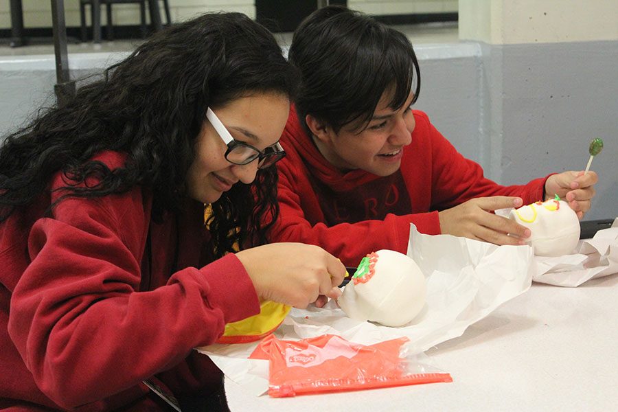 Leaning in for a better look, sophomore Araseli Ramos-Thaw, works hard on decorating her sugar skull as sophomore Irvin Xamora Galvan jokes around during first clubs. The club members were not the only students to decorate sugar skulls as Cheryl Loefflers Spanish III classes did so as well on Nov. 2.