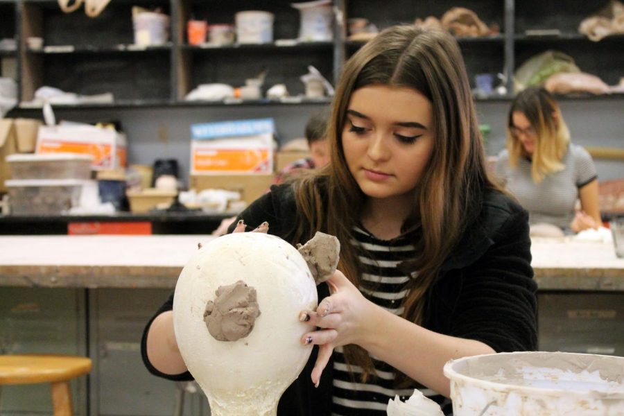 Creating her mask, junior Madison Simpson applies pieces of clay