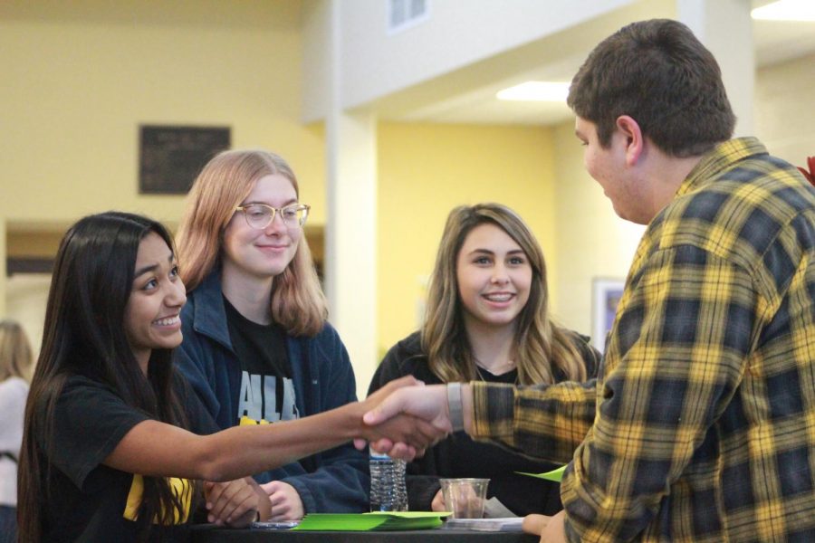 Juniors Alondra Valle and Eli Redington shake hands as Redington comes in to work the table with sophomores Daisy Buller and Jacey Yager.