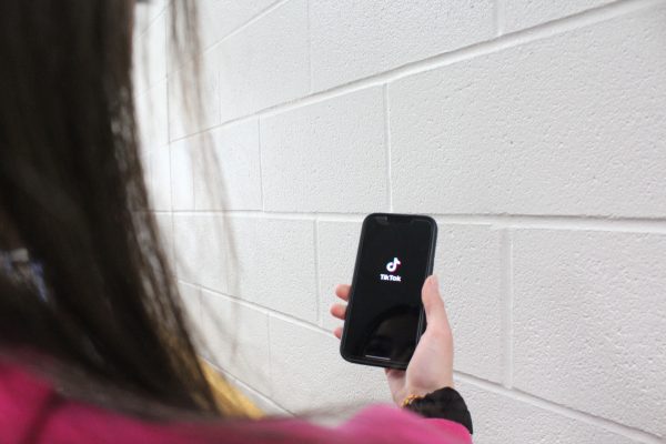 NHS student on their phone watching TikTok, while in the school hallway.